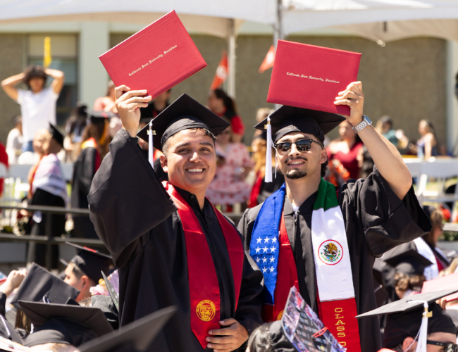 Two graduates holding their degrees